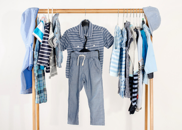 Dressing closet with clothes arranged on hangers.Blue and white wardrobe of newborn,kids, toddlers, babies full of all clothes.Many t-shirts,pants, shirts,blouses,blue hat, onesie hanging - Photo, image
