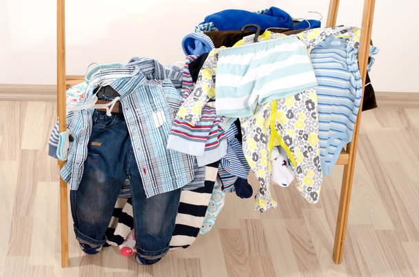 Wardrobe of newborn,kids, toddlers, babies.Many t-shirts,pants, shirts, shoes, hat,blouses, onesie in a pile . Messy clothes thrown on a shelf - Photo, image