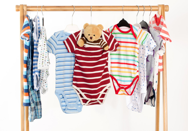Dressing closet with clothes arranged on hangers.Colorful onesie of newborn,kids, toddlers, babies on a rack.Many colorful t-shirts, shirts,blouses, onesie hanging, bear toy - Photo, Image