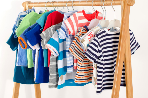 Dressing closet with clothes arranged on hangers.Colorful wardrobe of newborn,kids, toddlers, babies full of all clothes.Many t-shirts,pants, shirts,blouses, onesie hanging - Photo, image