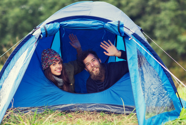 smiling couple of tourists looking out from tent - 写真・画像