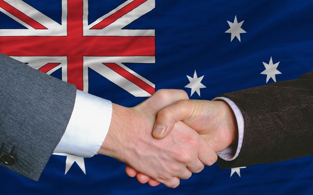 Geschäftsleute geben sich nach einem guten Deal vor der australischen Flagge die Hand - Foto, Bild