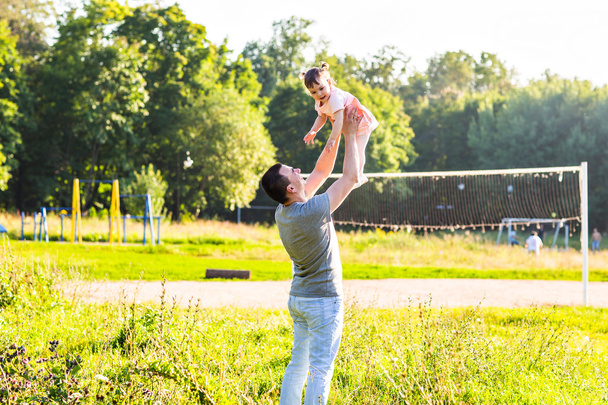 Pikkutyttö kävelee kesäpuistossa isänsä kanssa
 - Valokuva, kuva