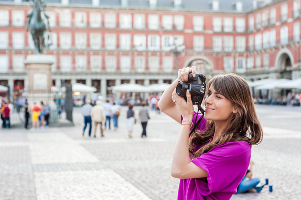 Jonge vrouw toeristische houden een fotocamera, zitten en kijken naar gebouwen in Plaza Mayor vierkante, Madrid, Spanje - Foto, afbeelding