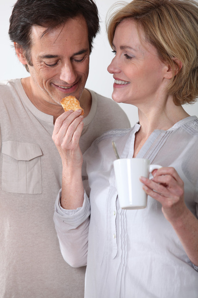 Woman with cup of coffee feeding her partner a biscuit - Foto, immagini