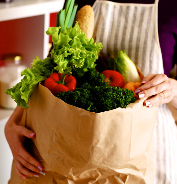 Frutas e legumes variados em saco de supermercado marrom segurando uma jovem
 - Foto, Imagem