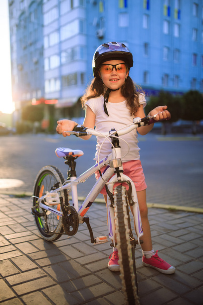 little girl with bicycle in summer park against sunset - Foto, immagini