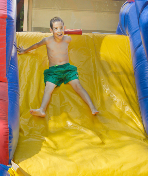 Мальчик наслаждается влажной надувной горкой
 - Фото, изображение