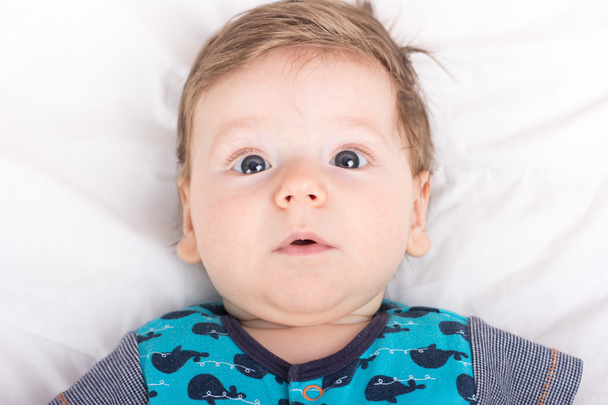 Portret van een glimlachend kind. Een kind op een witte bed. Knappe jongen. - Foto, afbeelding