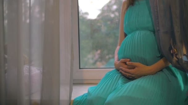 Kobieta w ciąży siedząc na parapecie i obejmując brzuch - Materiał filmowy, wideo