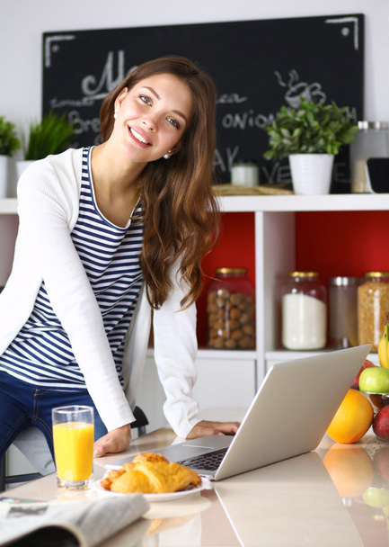Attractive young woman using laptop and sitting in the kitchen  - 写真・画像
