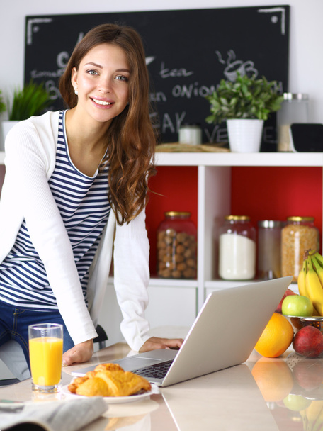 Attractive young woman using laptop and sitting in the kitchen  - Fotoğraf, Görsel