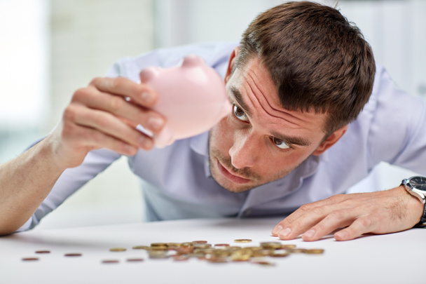 zakenman met piggy bank en munten op kantoor - Foto, afbeelding