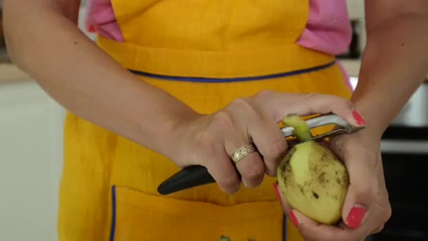 Μια γυναίκα με το πορτοκαλί μανικιούρ ξεφλούδισμα ένα πατάτες - Πλάνα, βίντεο
