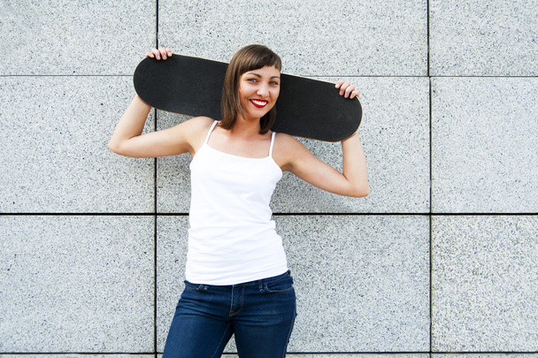 Young girl with skateboard on her shoulders in the city by the w - Photo, Image