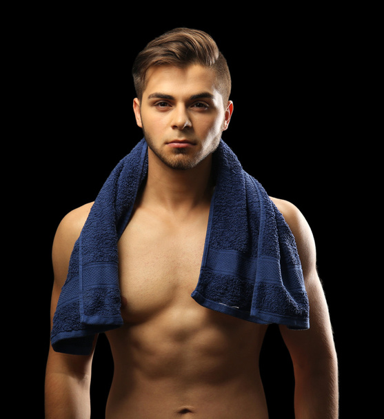 Muscle young man holding towel on dark background - Foto, Imagen