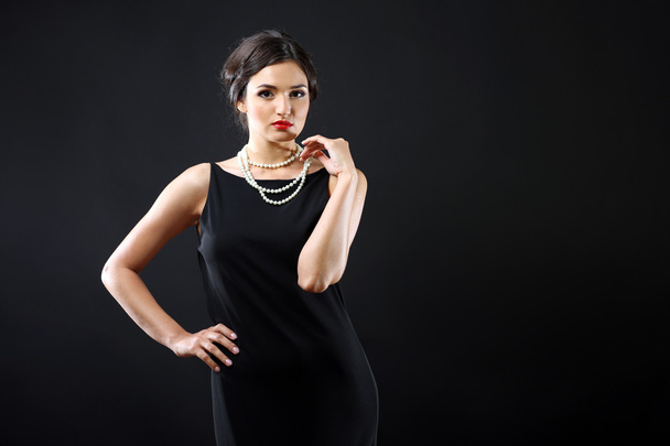 Pretty woman in black dress and white beads on dark background - Foto, Imagem