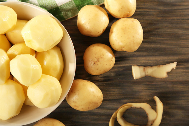 Peeled new potatoes in bowl on wooden table with napkin, top view - Fotoğraf, Görsel