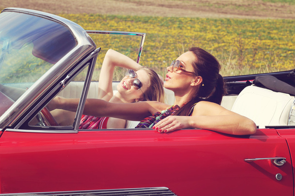 Beautiful ladies with sun glasses riding a vintage retro car - Photo, Image
