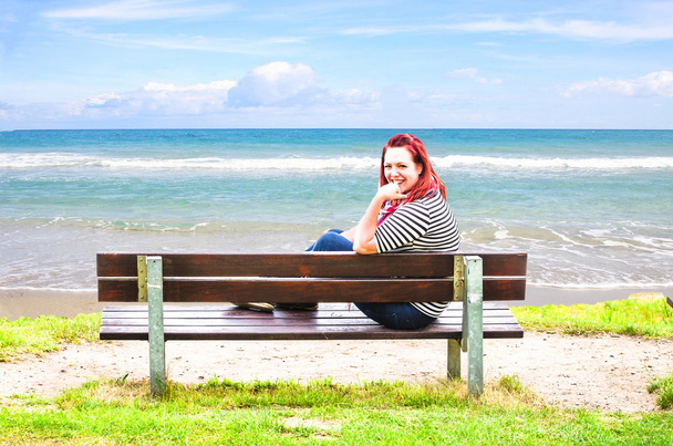 Νεαρή γυναίκα στον πάγκο, κοιτάζοντας έξω στη θάλασσα - Φωτογραφία, εικόνα