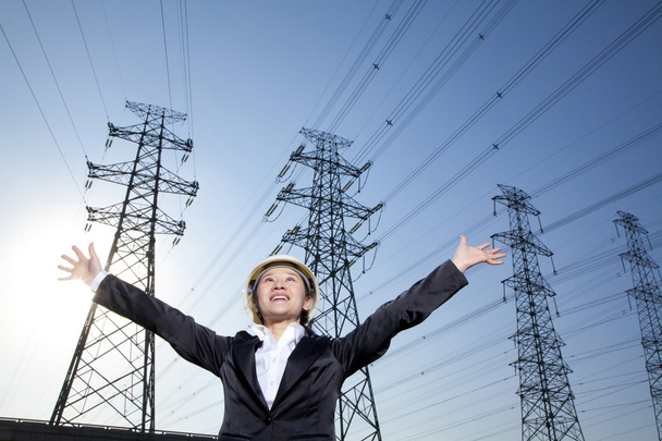 Mulher de negócios na frente de linhas de energia com os braços estendidos
 - Foto, Imagem