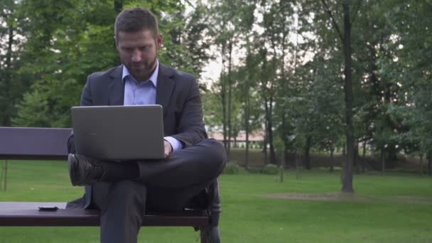 Üzletember dolgozik laptop, ül a padon a parkban. - Felvétel, videó