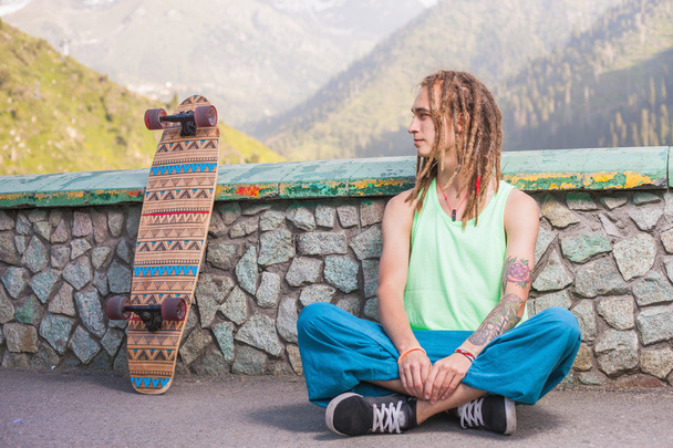 Portrait of cool, funny handsome man with skateboard at mountain - Foto, Bild