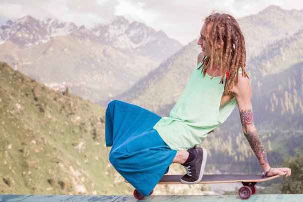Hippie young and handsome man with longboard skateboard at mountain - Φωτογραφία, εικόνα
