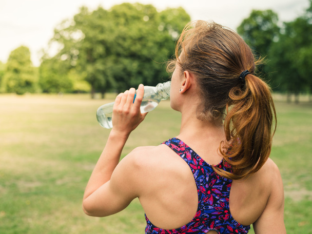 Sportliche Frau trinkt im Park aus Flasche - Foto, Bild