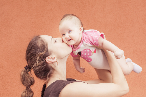 Happy mother kissing her baby at wall background - Фото, изображение