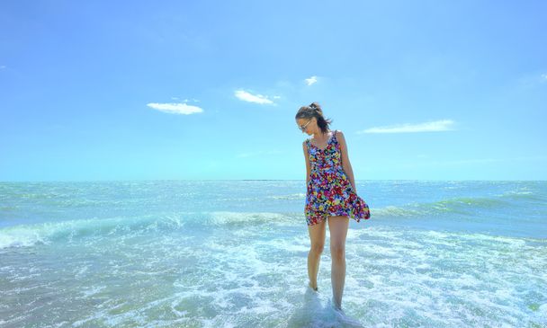 Jeune femme souriante debout dans les vagues de la mer et tenant sa robe
 - Photo, image