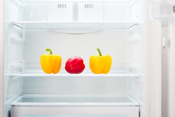 Dos pimientos amarillos y uno rojo en el estante del refrigerador vacío abierto
 - Foto, Imagen