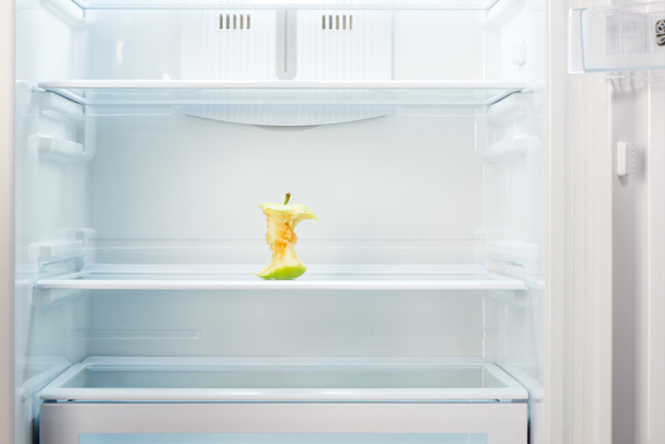 Apple core on shelf of open empty refrigerator - 写真・画像