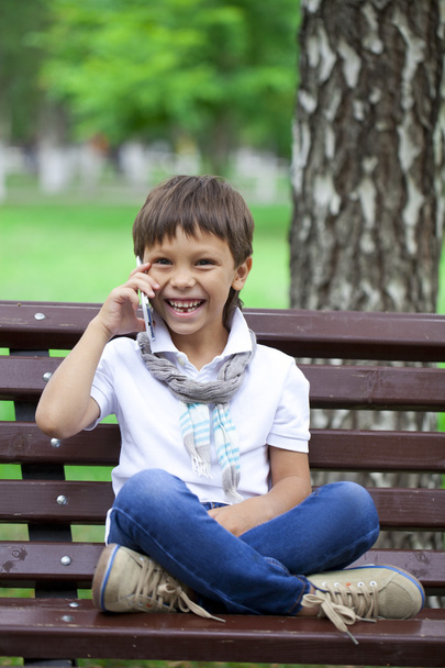 A little boy sits on a bench and calling by mobile phone  - Zdjęcie, obraz