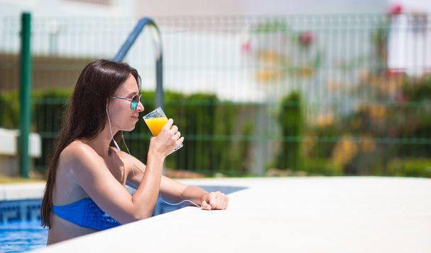 Young beautiful woman listening music with headphones near swimming pool - Photo, image