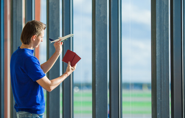 Καυκάσιος νεαρός εκμετάλλευση διαβατήρια και κάρτα επιβίβασης στο αεροδρόμιο κοντά σε παράθυρο - Φωτογραφία, εικόνα