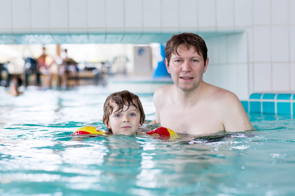 Nuori isä opettaa poikaansa uimaan sisätiloissa.
 - Valokuva, kuva