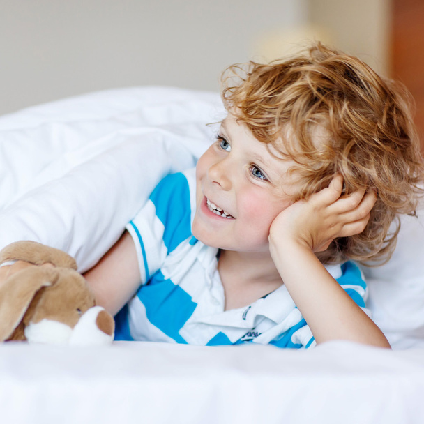 Adorable kid boy after sleeping in his white bed with toy - Fotó, kép