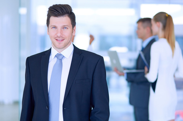 Portrait of young businessman in office with colleagues in the background - Foto, Bild