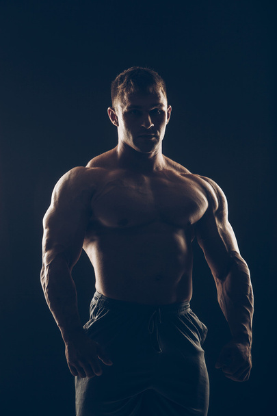 Handsome muscular bodybuilder posing over black background. - Photo, image