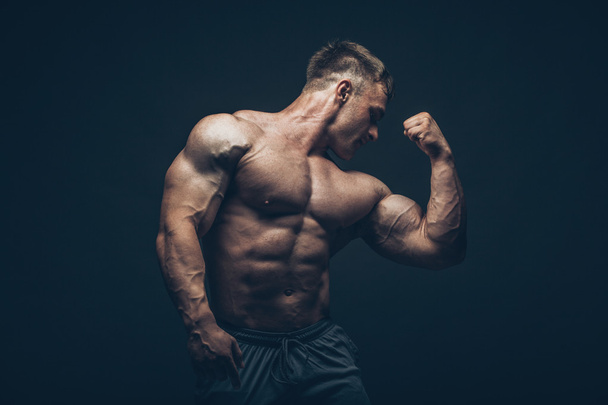Handsome muscular bodybuilder posing over black background. - Фото, изображение