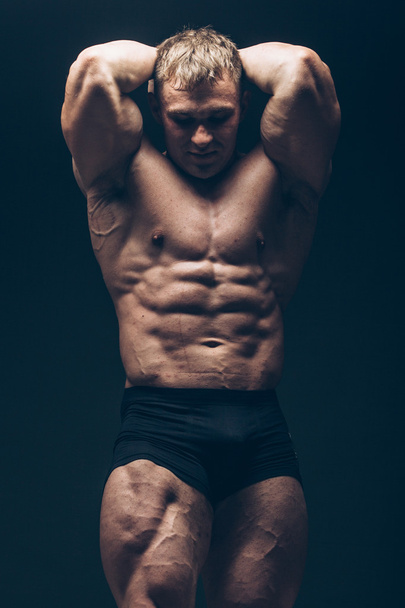 Beau bodybuilder musculaire posant sur fond noir
. - Photo, image