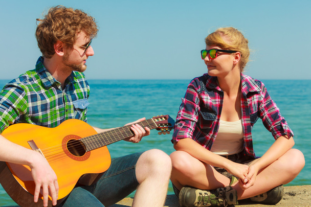 Young man playing guitar to his girlfriend by seaside - Foto, Imagen