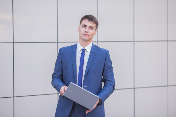 Successful businessman standing in the street holding a laptop - Foto, afbeelding