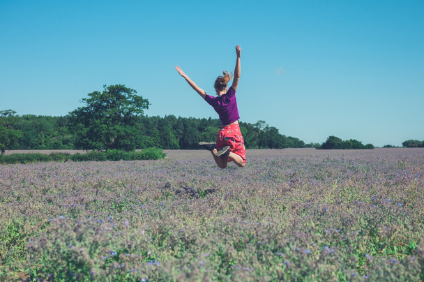 Jovem feliz pulando no campo de flores roxas
 - Foto, Imagem