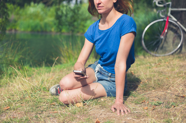 Νεαρή γυναίκα χρησιμοποιώντας έξυπνο τηλέφωνο από το νερό στο πάρκο - Φωτογραφία, εικόνα
