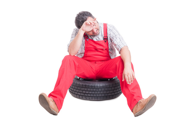 Cansado e exausto mecânico sentado em uma roda de carro
 - Foto, Imagem