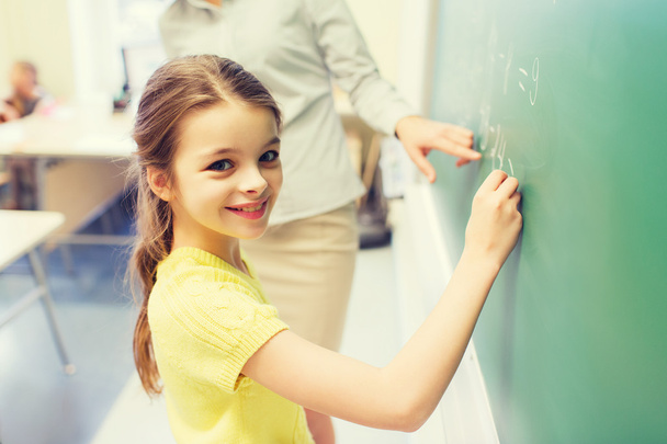 little smiling schoolgirl writing on chalk board - Foto, Imagem