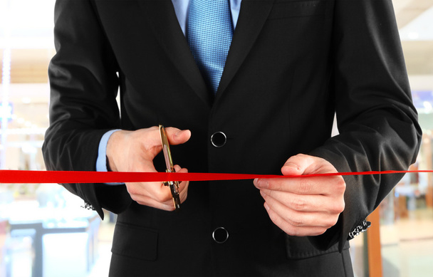 Businessman cutting red ribbon with pair of scissors close up - Foto, immagini