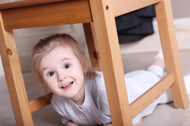 Little cute blond girl in striped shirt on floor under stool - Φωτογραφία, εικόνα